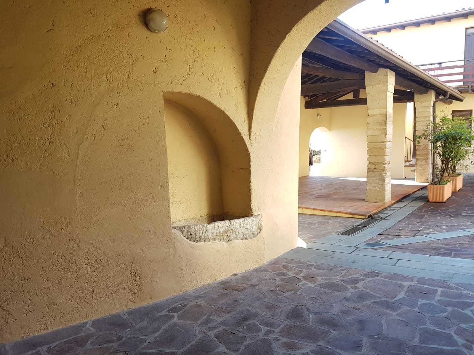 Ein überdachter Außenbereich mit Steinböden, einer gelben Wand und einem kleinen Fenster.