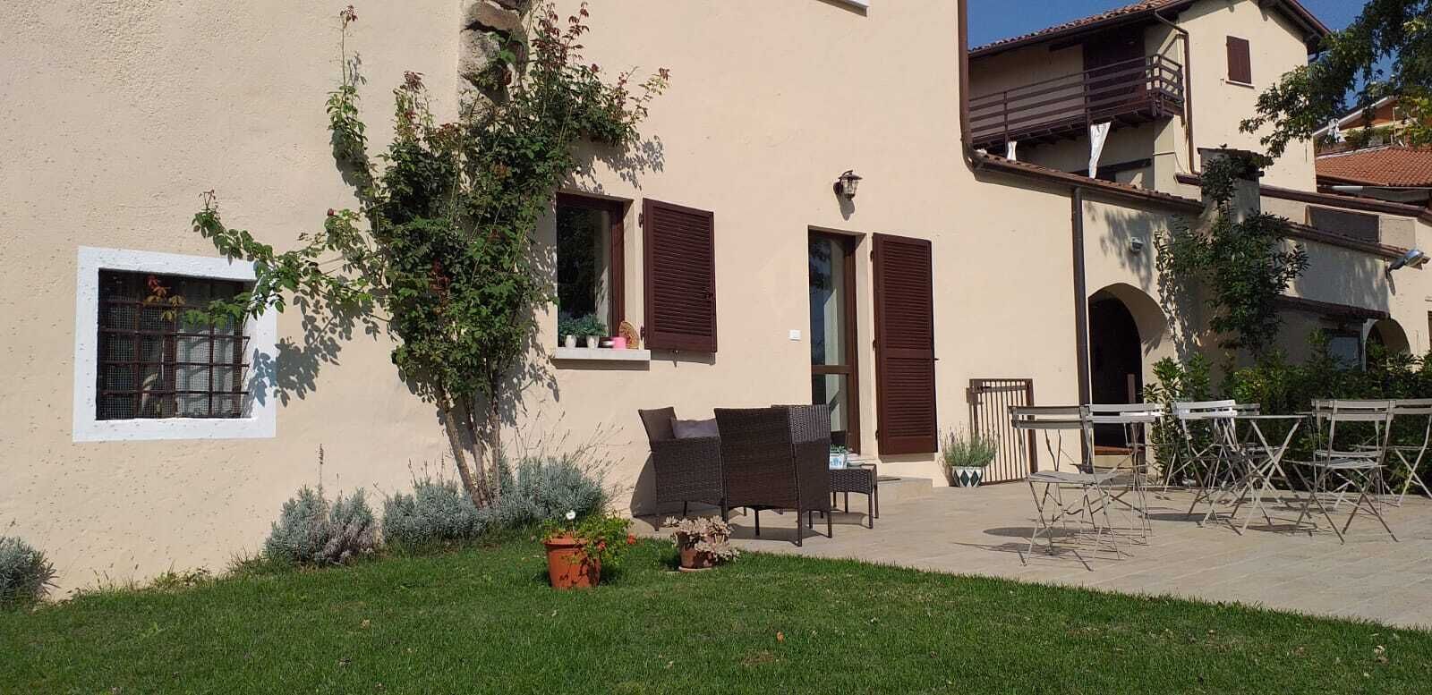 Ein hellbeiges Gebäude mit Balkon, kleinem Fenster und einer Tür. Ein Garten mit Rasen und einem Baum ist vorhanden.
