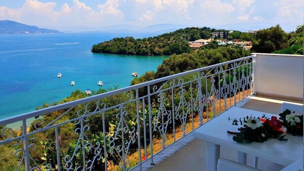 A balcony with a white railing overlooking a coastal view with boats, greenery, and buildings in the distance. - Dimitra Apartments and Studios Gouvia (Corfu)