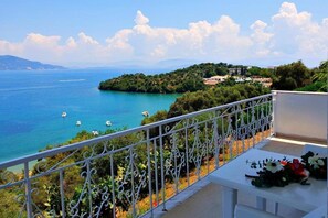 A balcony with a white railing overlooking a coastal view with boats, greenery, and buildings in the distance. - Dimitra Apartments and Studios Gouvia (Corfu)