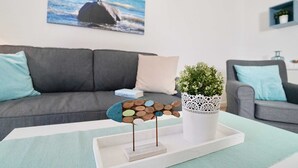 A living room with a grey sofa, a coffee table with a decorative fish sculpture, a potted plant, and a framed picture of a beach scene. - Holiday apartment (6) Zudar - Apartment house Johanneshorst (Sellin)