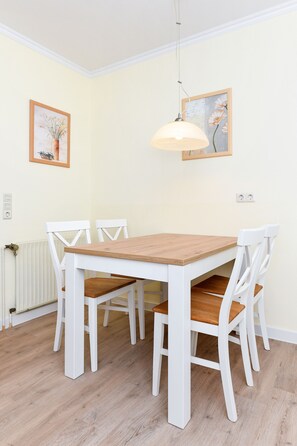 Un coin repas avec une table en bois et des chaises blanches, un luminaire suspendu et deux tableaux encadrés au mur.