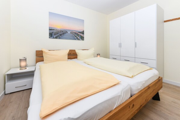 Une chambre avec un lit en bois, une armoire blanche et un tableau représentant un coucher de soleil accroché au mur.