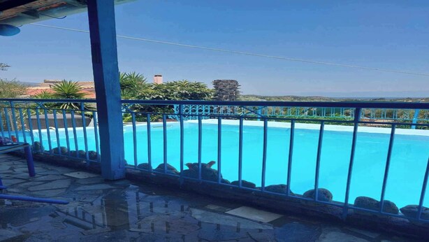 Una piscina azul cristalina con un patio de piedra y barandilla de metal.