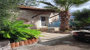 Un edificio de piedra con puerta y ventanas, una palmera y un coche estacionado al frente.