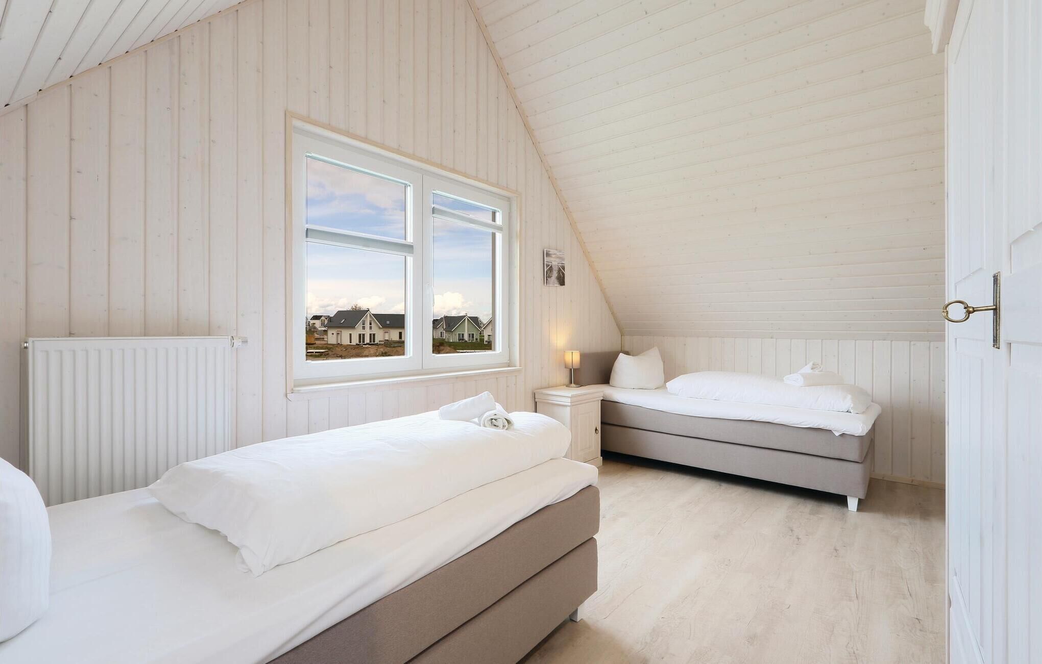 A bedroom with two beds, a window with a view of houses, a radiator, and a door with a keyhole.