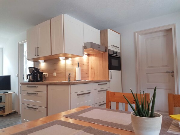 Une cuisine moderne avec des meubles en bois, un four encastré et un coin repas comprenant une table et des chaises.