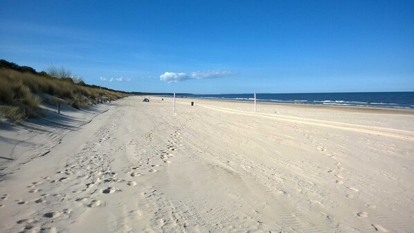 A sandy beach with footprints and a tent in the distance.