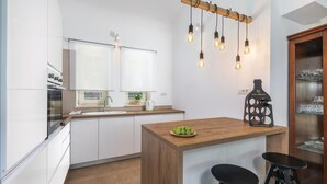 A modern kitchen with white cabinets, a wooden island, hanging light bulbs, a kettle, and a wine bottle on the counter. - Cozy home in Visnjan with sauna (Visnjan)