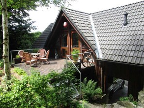 Une cabane en bois avec un toit en pente, une terrasse dotée de mobilier d’extérieur et une brouette.