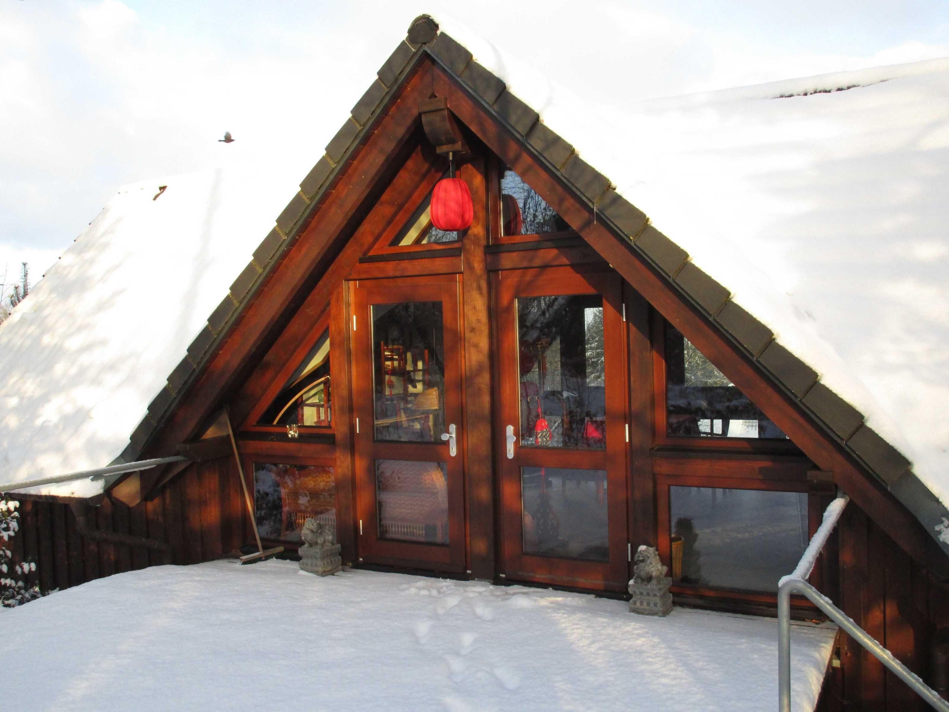 A wooden cabin with a triangular roof, large windows, and a snow-covered ground.