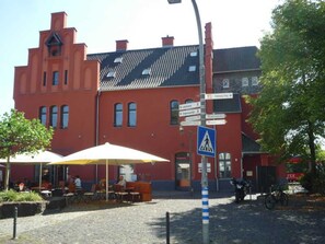 A red building with a pointed roof, a pedestrian crossing sign, and outdoor seating with umbrellas. - Vacation home in the countryside (with e-car charging station) - Holiday home in the countryside (Morsbach)