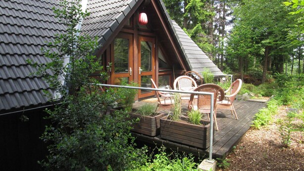 A cabin with a sloped roof, wooden deck, and outdoor seating area.