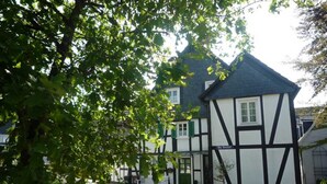 A traditional half-timbered building with a cobblestone courtyard, a white fence, and a bench.
