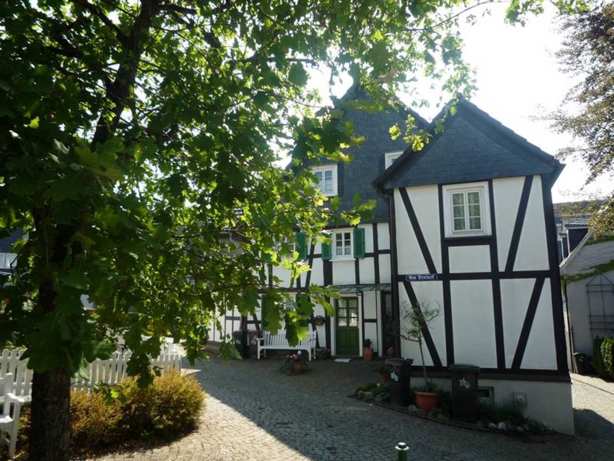 A traditional half-timbered building with a cobblestone courtyard, a white fence, and a bench.