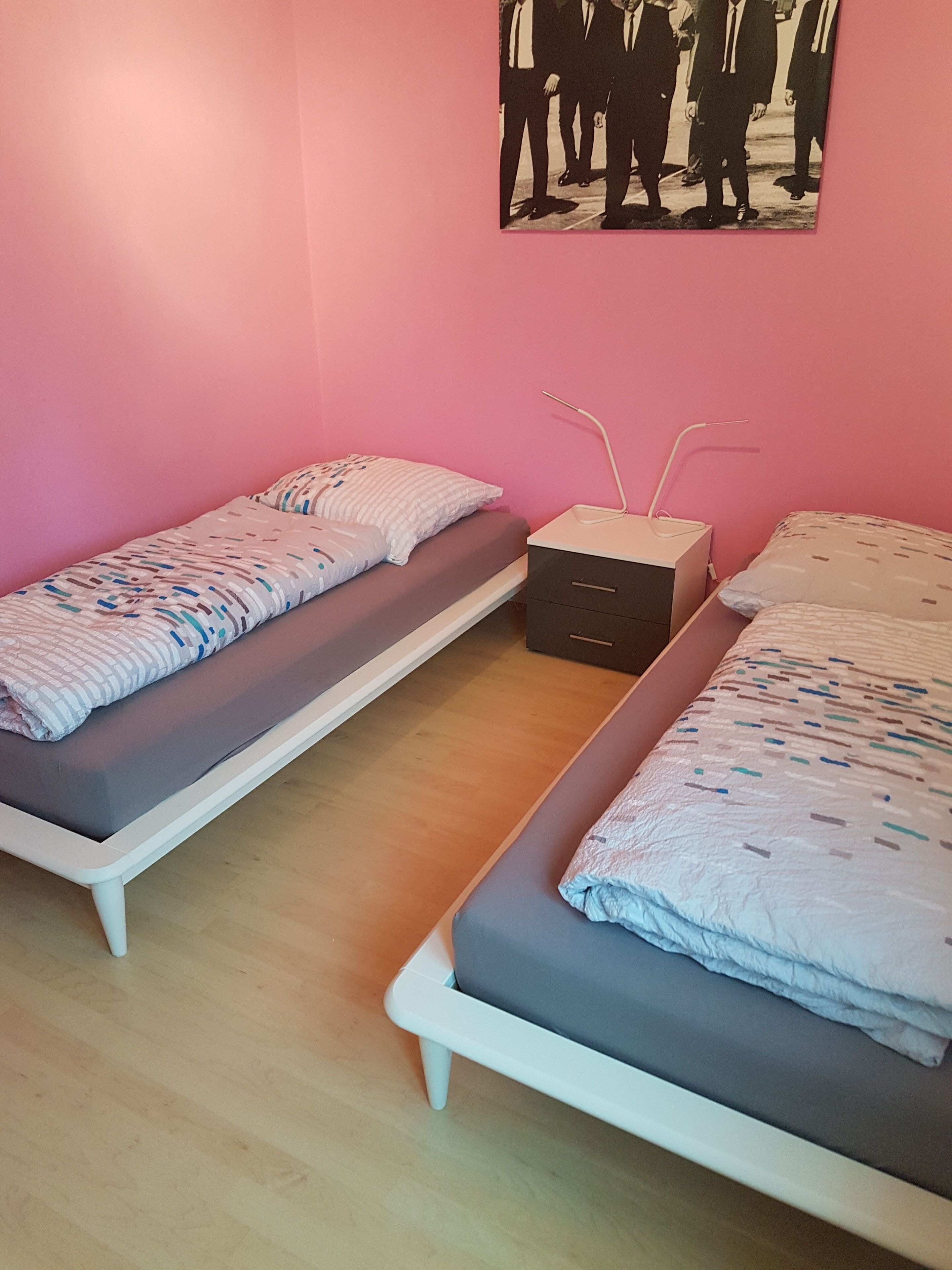 A room with two single beds, a bedside table with a lamp, and a wall-mounted picture.