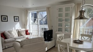 Uma sala de estar com sofá, poltrona estofada, televisão e mesa de jantar com cadeiras.