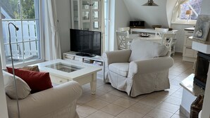 Uma sala de estar ampla com uma grande janela, televisão, área de jantar e lareira.