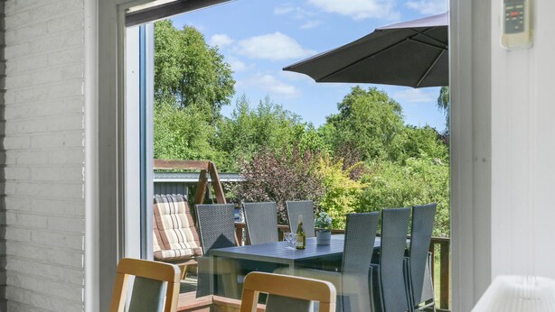 A patio with a table and chairs, a wooden swing, and a view of a garden with trees and shrubs. - 3 bedroom lovely home in Vig (Vig)