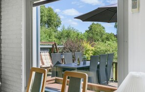 Une terrasse avec une table et des chaises, une balançoire en bois et une vue sur un jardin agrémenté d’arbres et d’arbustes.