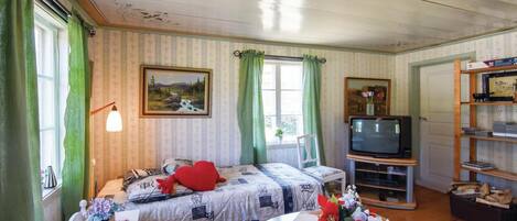 Um quarto aconchegante com duas camas, uma televisão, uma mesa com um vaso de flores e uma estante de livros.