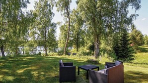 An outdoor seating area with wicker furniture, a view of a lake, and trees in the background. - Gorgeous home in Ambjörnarp with WiFi (Ambjörnarp)