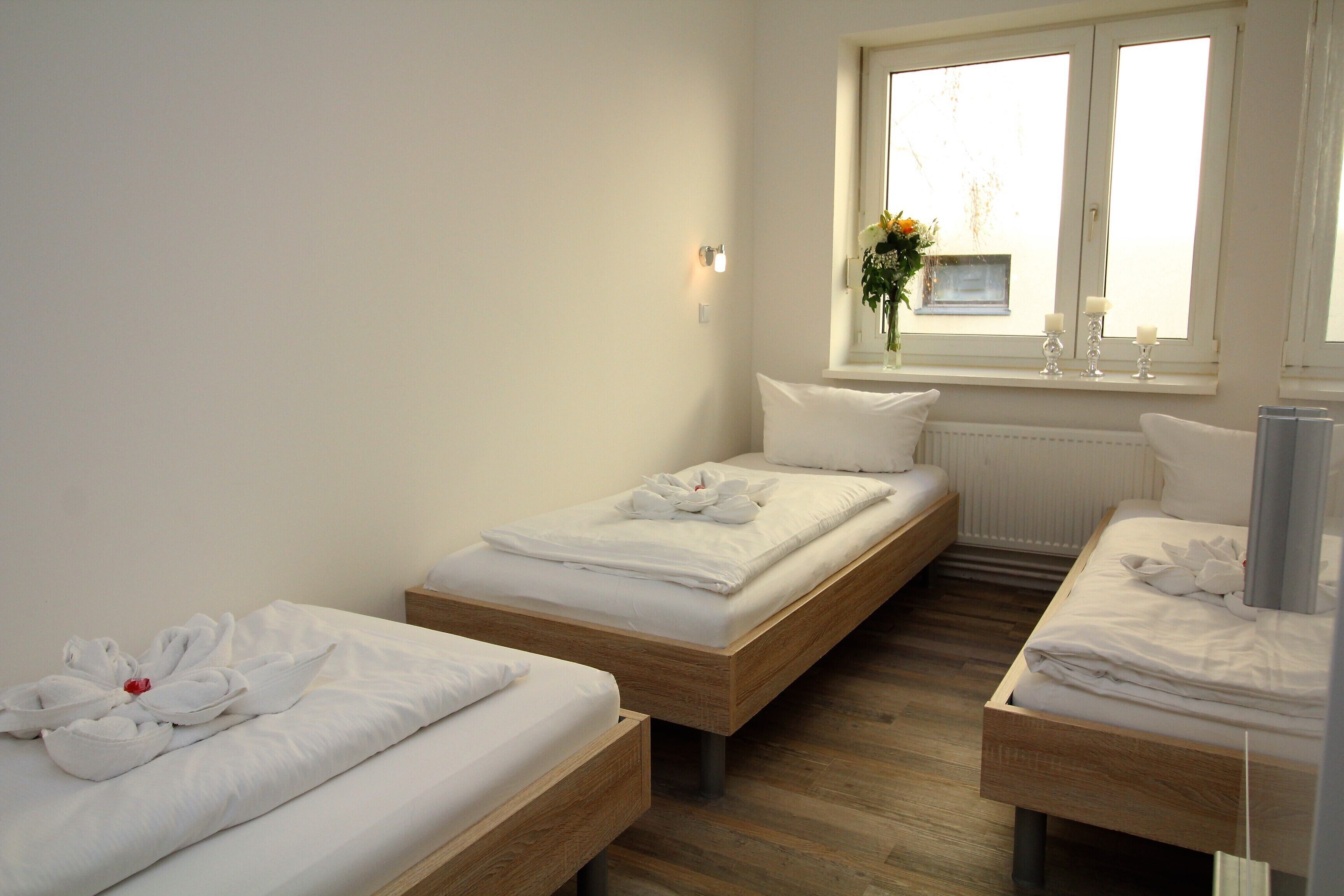 Ein Hotelzimmer mit zwei Einzelbetten, Holzboden, einem Fenster mit Blick und einer Vase mit Blumen auf der Fensterbank.