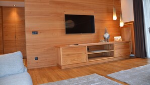 A modern living room with a wooden wall, a flat-screen TV, a wooden entertainment unit, and a grey sofa. - Exclusive mountain lodge style apartment - 90 m² - Free WIFI (Ortisei)