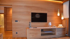 A modern living room with a wooden wall, a flat-screen TV mounted above a wooden console, and pendant lighting. - Exclusive mountain lodge style apartment - 90 m² - Free WIFI (Ortisei)