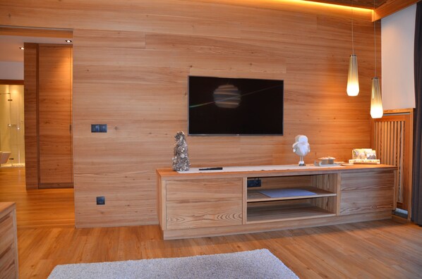Ein modernes Wohnzimmer mit einer Holzwand, einem flachbildfernseher, der über einer Holzkonsole angebracht ist, und Pendelleuchten.