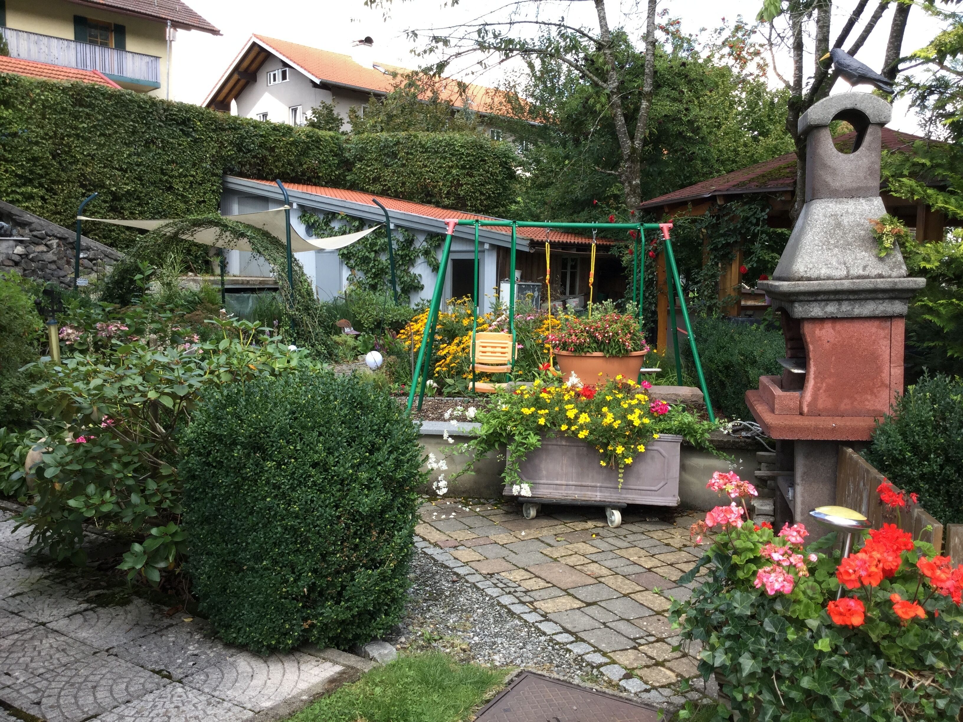 A garden with a swing set, potted plants, and a bird feeder.