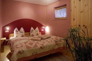 Une chambre à coucher avec un lit, une table de chevet, une fenêtre avec des rideaux et une porte en bois.