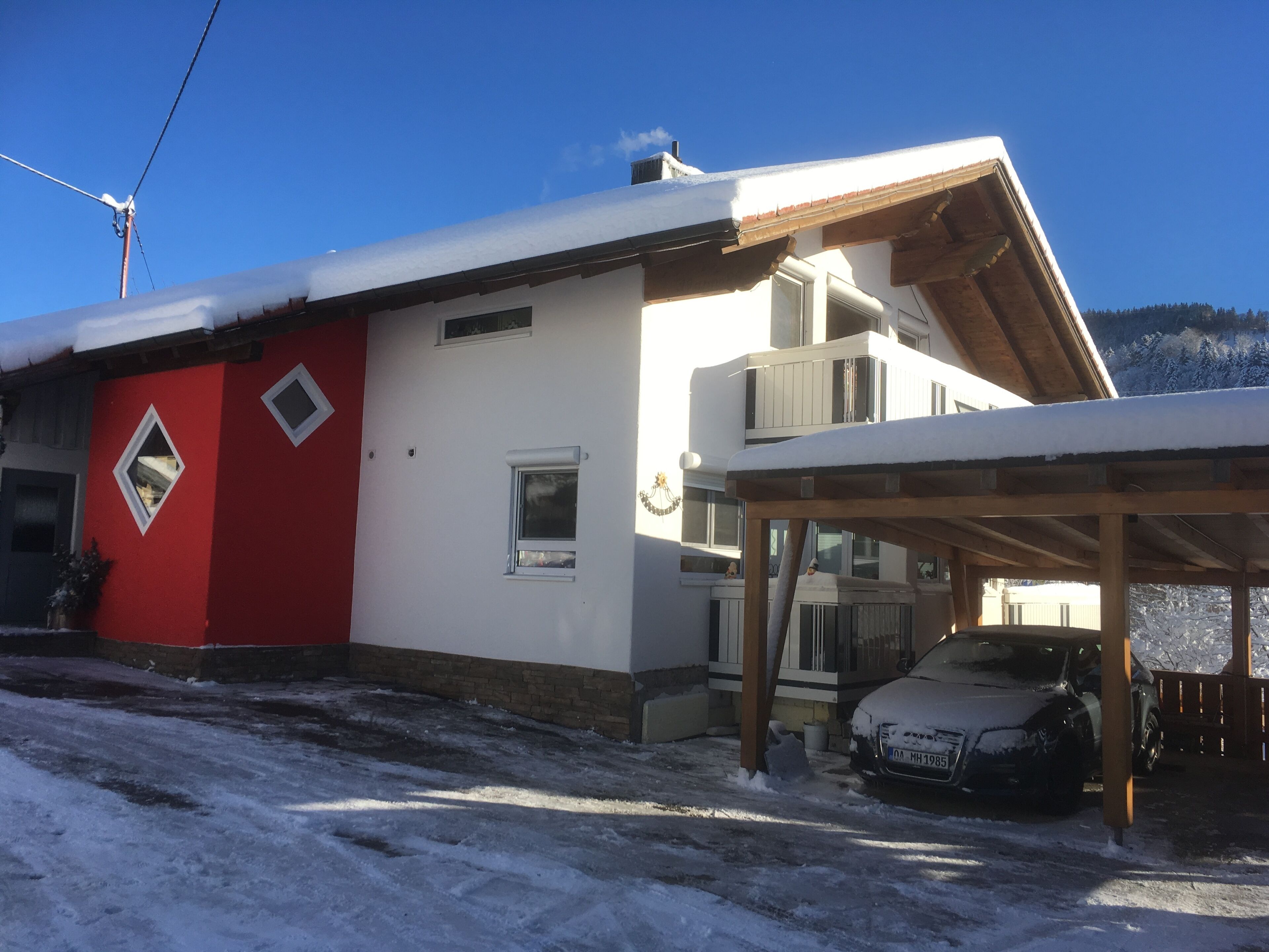 Casa de dos pisos con fachada roja y blanca, un porche cubierto y un coche estacionado adelante.