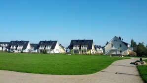 Um bairro residencial com casas, um campo gramado e um caminho de terra.
