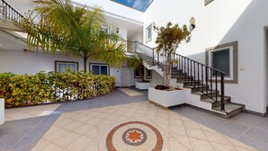 A spacious indoor area with a tiled floor, a staircase with a black railing, and a variety of potted plants. - Nice, modern apartment on the beach with sea view & terrace, free WiFi (Puerto de Mogan)