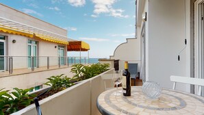 A balcony with a tiled table, a bottle of wine, and a glass, overlooking a pool and a building with a yellow awning. - Nice, modern apartment on the beach with sea view & terrace, free WiFi (Puerto de Mogan)