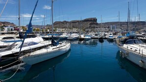 A marina with multiple sailboats docked, calm water, and a mountainous backdrop. - Nice, modern apartment on the beach with sea view & terrace, free WiFi (Puerto de Mogan)