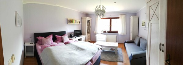 Ein Schlafzimmer mit einem Bett, einem Schreibtisch, einem Sessel, einer Couch und einem Kleiderschrank.