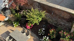 Un espace extérieur aménagé en patio, avec un mur en briques, des plantes en pot et du mobilier d’extérieur.