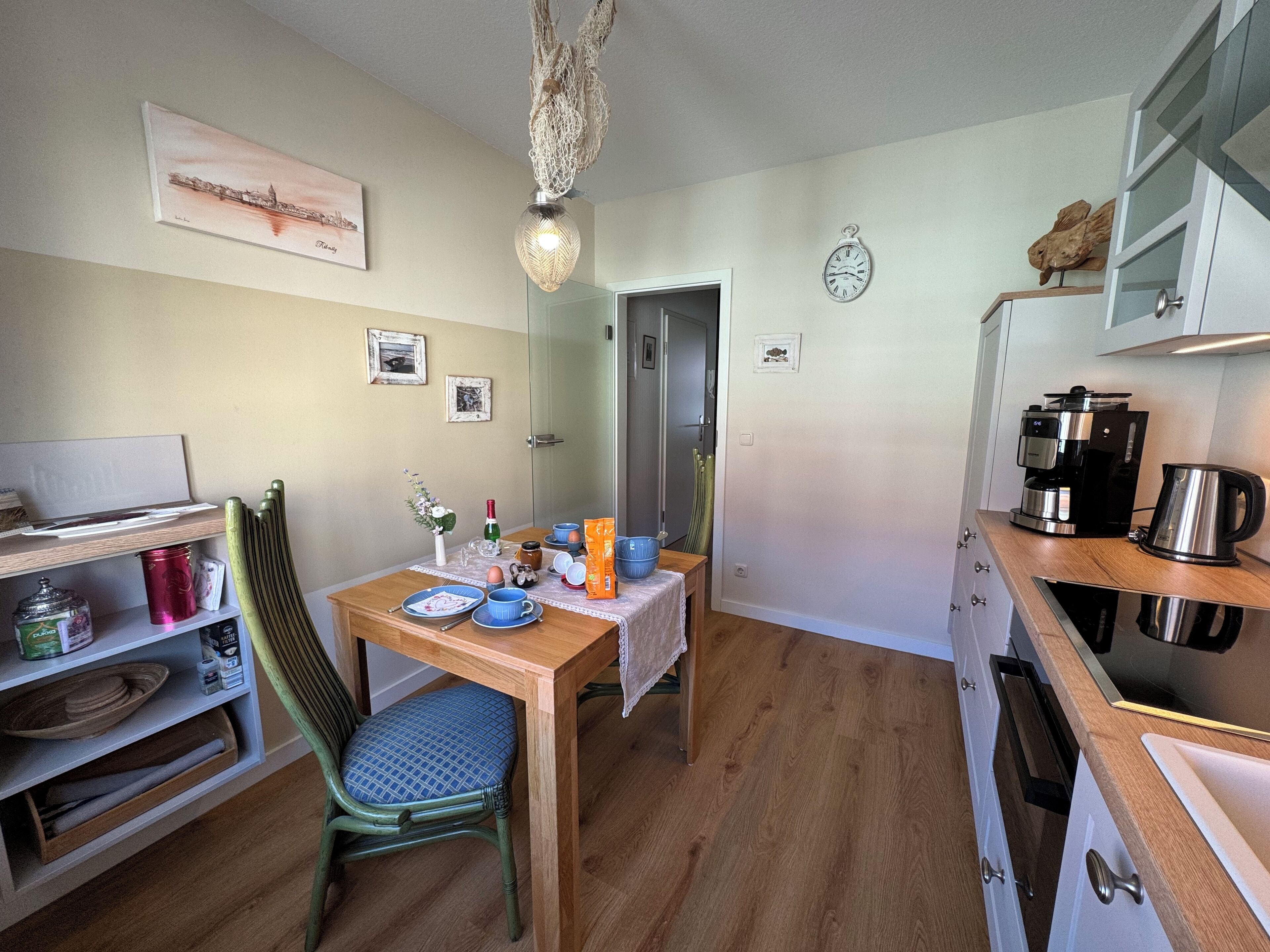 Una cocina compacta con armarios de madera, una mesa de comedor con platos azules, una cafetera y un accesorio de luz decorativo.