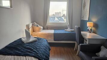 Habitación de hotel con dos camas, un escritorio, una silla y vistas a edificios a través de la ventana.