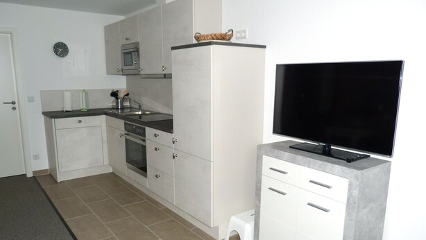 Cocina compacta con microondas, horno y una televisión de pantalla plana sobre un soporte.