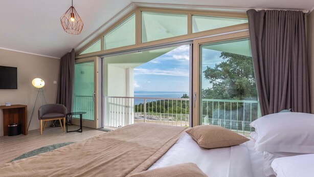 Une chambre à coucher avec un grand lit, une chaise, un bureau et une vue sur l’extérieur grâce à une porte vitrée.