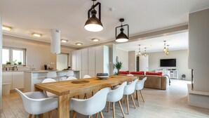 Une cuisine moderne avec une table à manger en bois, des chaises blanches et des luminaires suspendus.