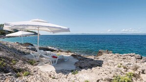 A rocky beach with white lounge chairs and umbrellas, overlooking a clear blue sea. - Gorgeous home in Prigradica with sauna (Prigradica)