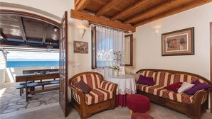 A cozy room with a wooden ceiling, a large window with curtains, a wooden bench, two patterned sofas, a small round table, and a view of the sea. - Gorgeous home in Prigradica with sauna (Prigradica)