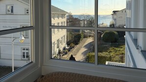 A room with a large window overlooking a street, wicker furniture, and a lamp.