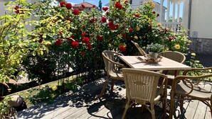 A patio with wicker furniture and a table, surrounded by a garden with red and yellow roses.