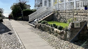 A white building with a stone staircase leading to a balcony, a cobblestone path, and a clear sky.