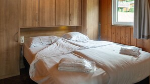 Una cama bien hecha con sábanas y toallas blancas, paredes de madera y una ventana con cortinas.
